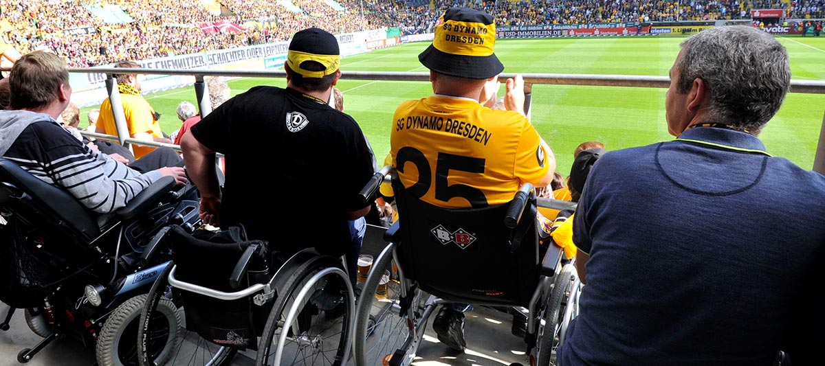 Fans verfolgen im Rollstuhl ein Fußballspiel